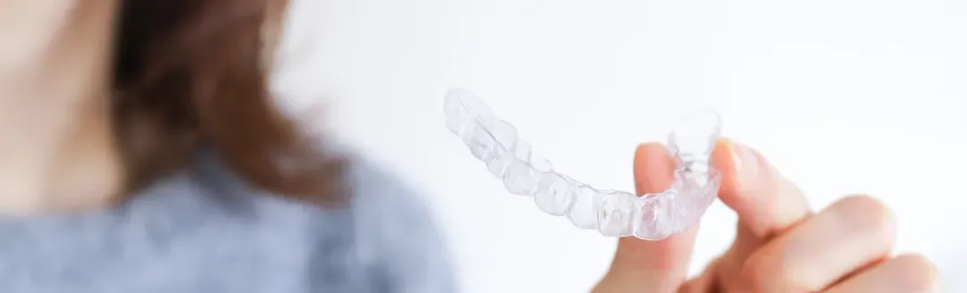 Woman holding clear dental aligner or retainer against white background