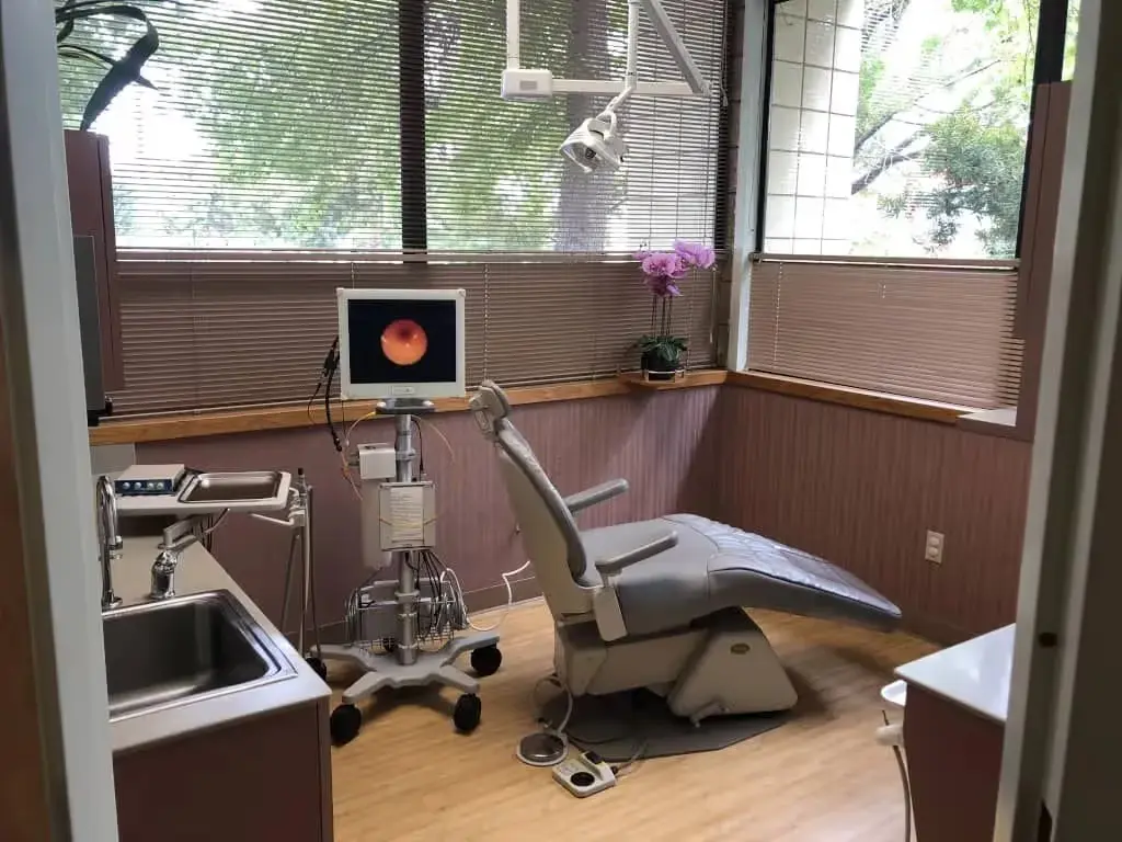 Modern dental operatory with chair, overhead light, equipment, and large windows in clinical setting.
