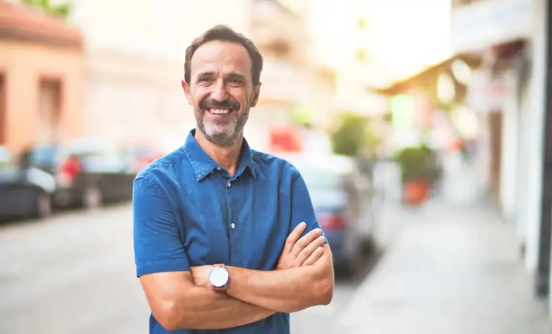Professional man in blue shirt with arms crossed, standing outdoors on residential street.